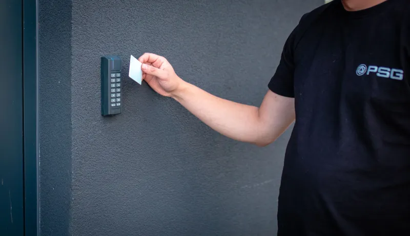 Instalator w koszulce PSG przykłada kartę do czytnika kontroli dostępu przy wejściu.