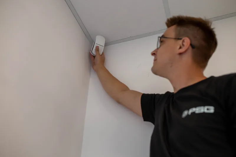 Instalator PSG montuje czujkę alarmową w narożniku pomieszczenia.